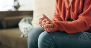 Woman anxiously gripping hands together wearing orange sweater and jeans
